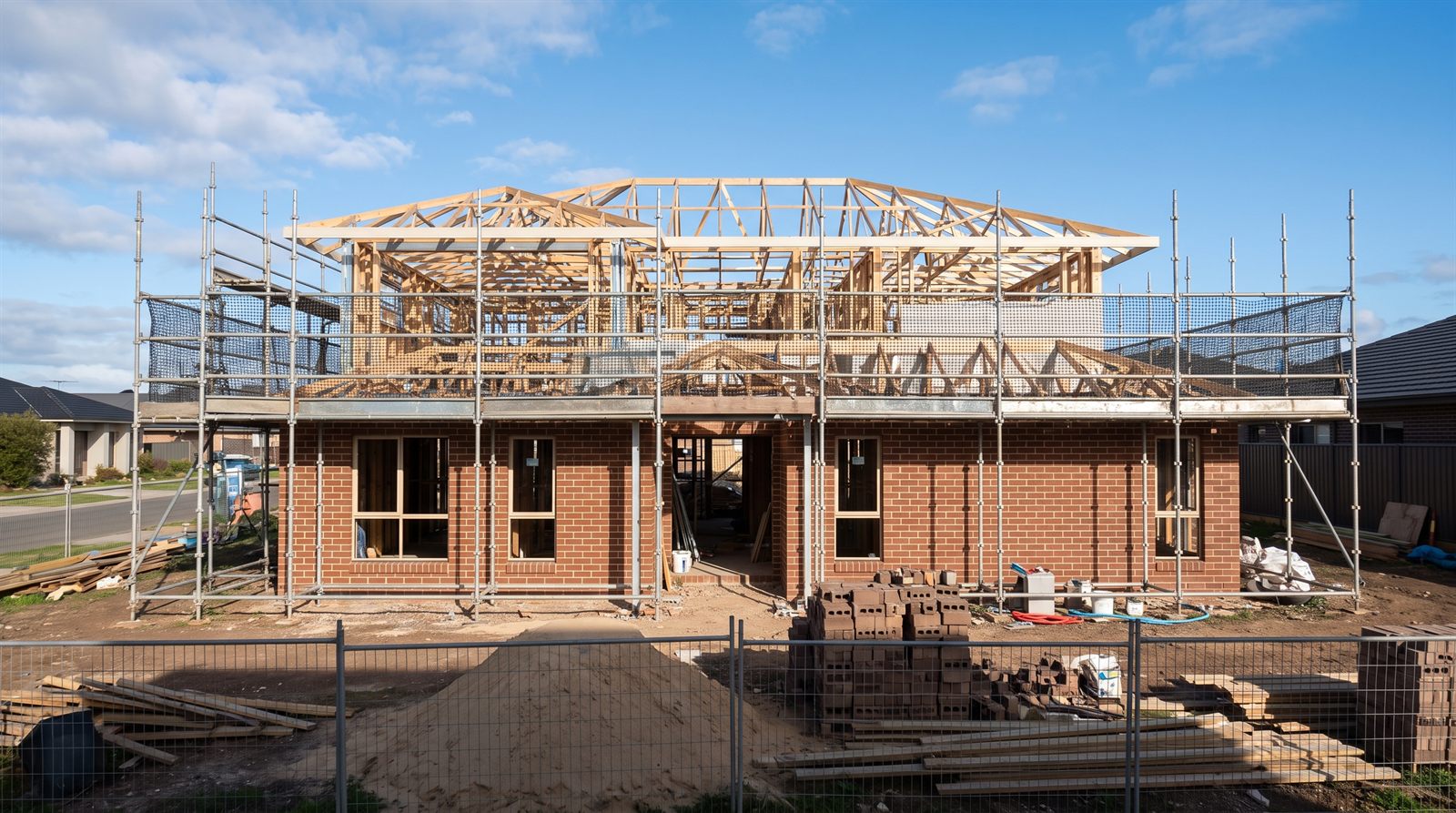 Double-storey brick home under construction with roof trusses and scaffolding
